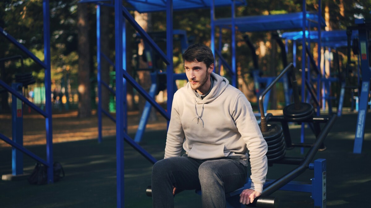 Imagen de un hombre de mediana edad sentado en un banco del gimnasio tras entrenar, representando la frustración de no perder grasa aunque se esté en déficit calórico.